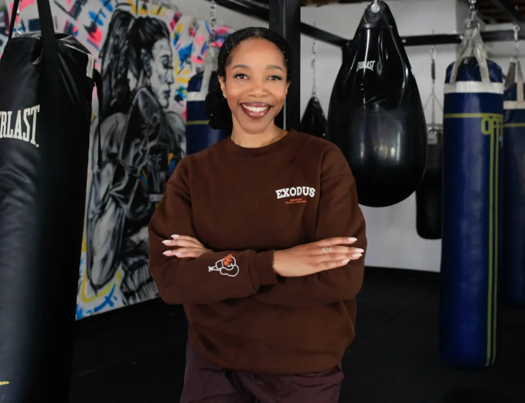 Desiree Tanner smiling in a boxing gym to symbolize fighting back against cancer, wearing the Exodus Sweatshirt